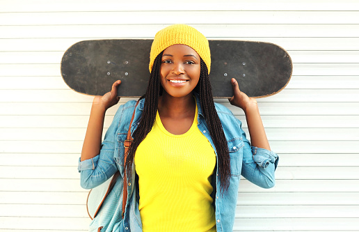 Fashion pretty young smiling african woman with skateboard in colorful clothes over white background