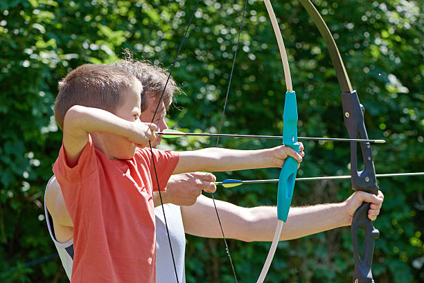 Little boy and man with big bow shooting Little boy and man with big bow shooting in sunny summer day archery photos stock pictures, royalty-free photos & images