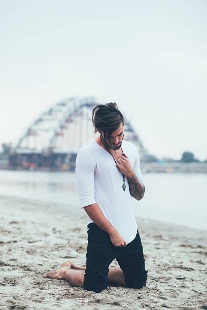 Sad man kneeling on sand by the river