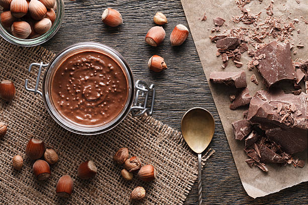 Hazelnut spread with nuts pieces A still life with a hazelnut spread glass jar, milk chocolate and hazelnuts. Top view. hazelnut stock pictures, royalty-free photos & images