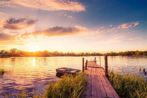 Sunset over the lake in the village. View from a wooden bridge, image in the orange-purple toning