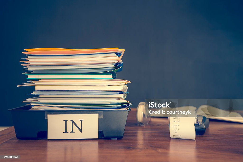 Large stack of paperwork and files with calculator. Large stack of paperwork and files with calculator. An assortment of files and booklets and paper in an in tray on a desk. There is also an adding machine calculator. There are no people. Stress, overwork and finance concept. Paper Stock Photo