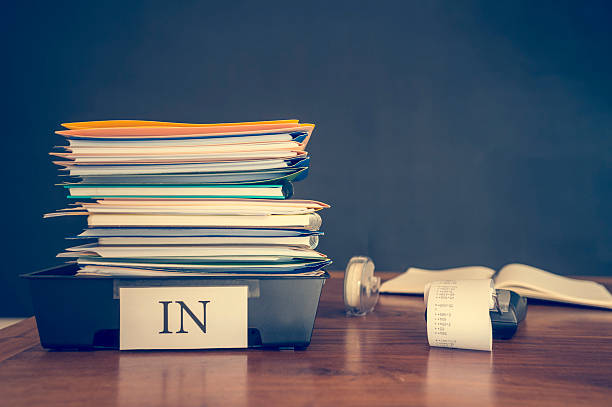 Large stack of paperwork and files with calculator. Large stack of paperwork and files with calculator. An assortment of files and booklets and paper in an in tray on a desk. There is also an adding machine calculator. There are no people. Stress, overwork and finance concept. inbox filing tray stock pictures, royalty-free photos & images