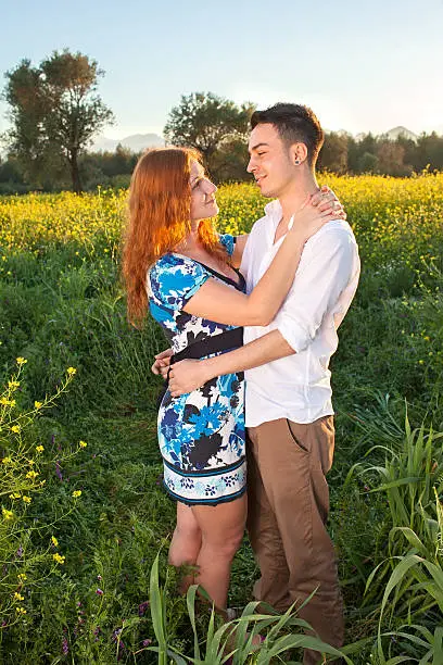 Romantic young couple enjoy a tender moment standing smiling and looking lovingly into each others eyes in the evening light in a field of colorful yellow rapeseed flowers.