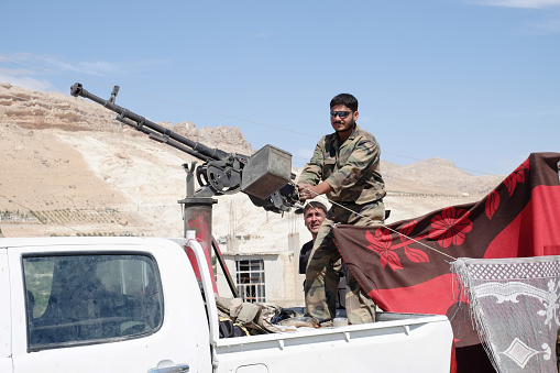 Ma'loula, Syria - September 19, 2013: The soldiers of the Syrian National Army at the checkpoint near the gate in Maaloula holding a machine gun mounted on a pick-up truck. Maaloula became a place of fighting between Assad forces and the rebels.