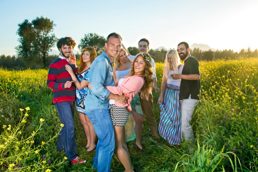 Four happy young couples having a party in the countryside dancing and laughing together in a colorful yellow rapeseed field.