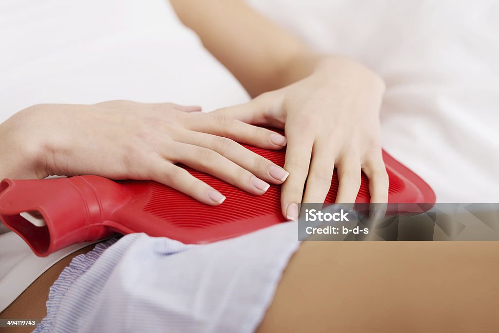 Beautiful caucasian woman lying with hot water bag Beautiful caucasian woman lying in bed with hot water bag and holding it on her belly. Heat - Temperature Stock Photo