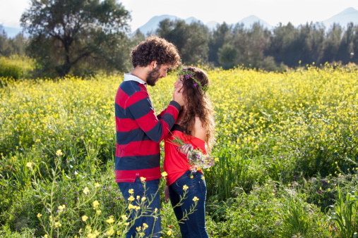 Loving young couple in a yellow rapeseed field standing looking tenderly into each others eyes on a sunny summer day.