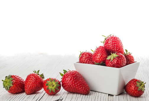 Fresh strawberries in a bowl on white rustic background with copy paste