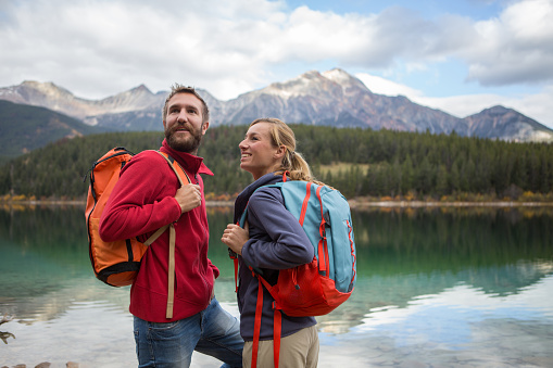 Young cheerful couple hiking by the lake in Autumn, they are having a break looking at the beautiful landscape.