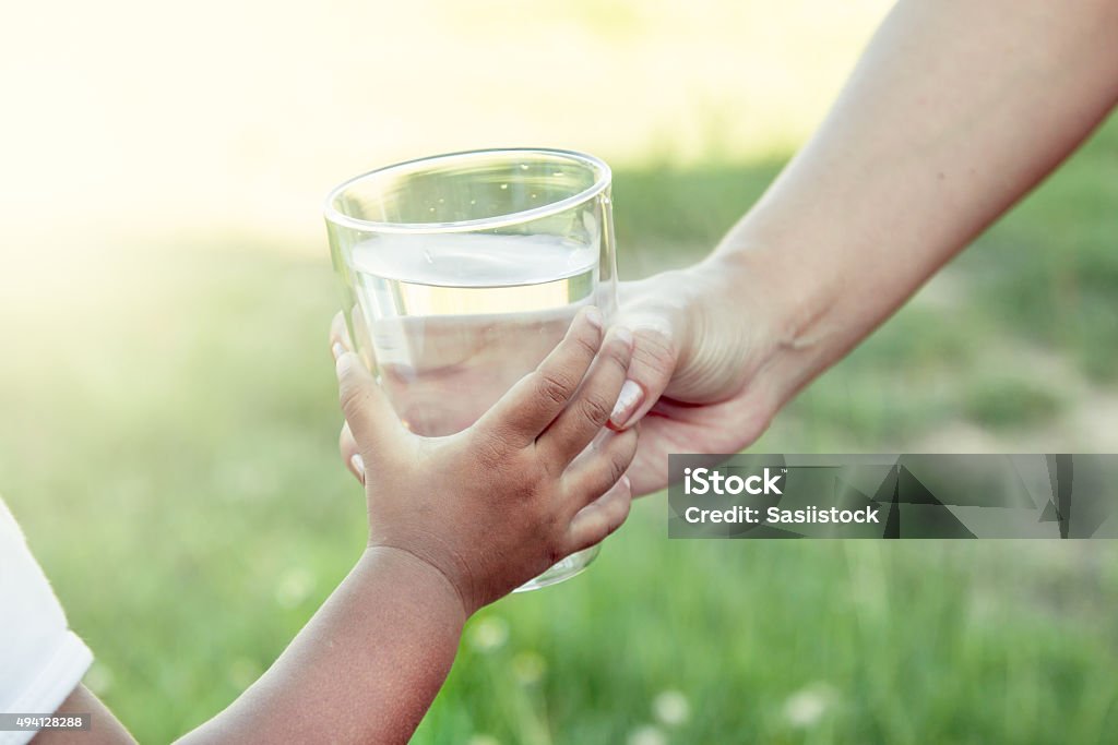 Woman hand giving glass of fresh water to child Woman hand giving glass of fresh water to child in the park,soft color filter Child Stock Photo