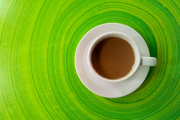 A white cup of coffee and scattered coffee beans.