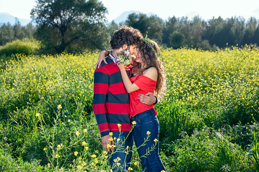 Young couple enjoying a romantic kiss as they stand in a field of yellow rapeseed flowers on a sunny summer day.