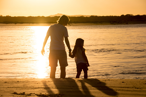 Mother and daughter at the beach, holding hands watching the sunset.