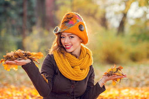 Portrait of happy teenage girl holding leaves in her hands and enjoying in nature during autumn.