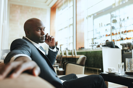 African business man talking on mobile phone while waiting in a hotel lobby. Young business executive using cell phone while waiting at lounge.