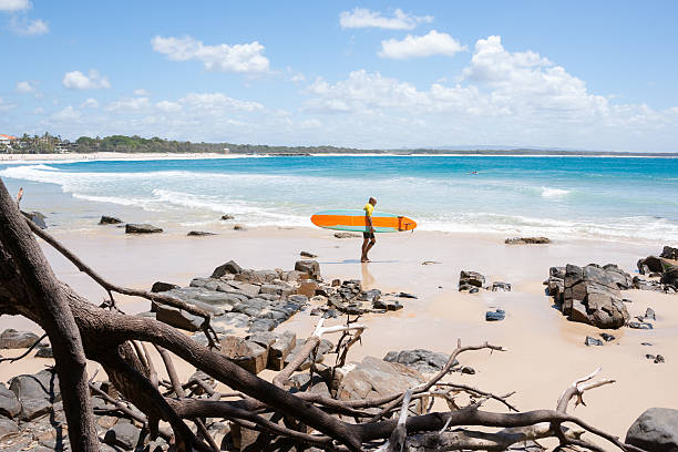 Noosa, Australia - March 11, 2014: Surfer carrying a yellow longboard heads to the water to complete in the Noosa Festival of Surf . The festival is an annual event.at attracting surfers from around the world.