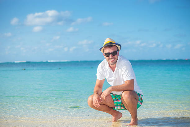 casual homme debout accroupi sur une plage tropicale - crouching male men sensuality photos et images de collection