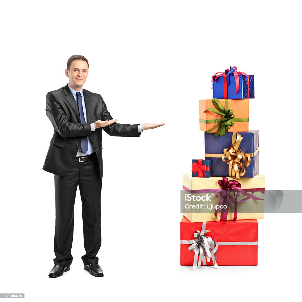 Man in suit gesturing and pile of gifts Full length portrait of a man in suit gesturing and pile of gifts isolated on white background Gift Stock Photo