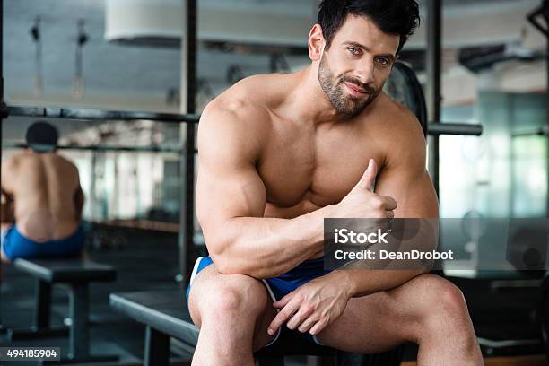 Muscular Man Sitting On The Bench And Showing Thumb Up Stock Photo - Download Image Now