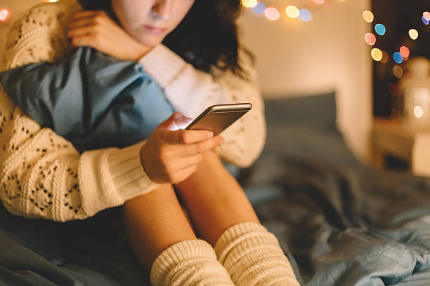girl in bed using phone - meisjes stockfoto's en -beelden