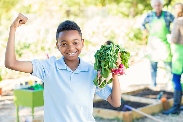 ragazzo mostrando i muscoli con verdure nel giardino durante campo viaggio - school farm foto e immagini stock