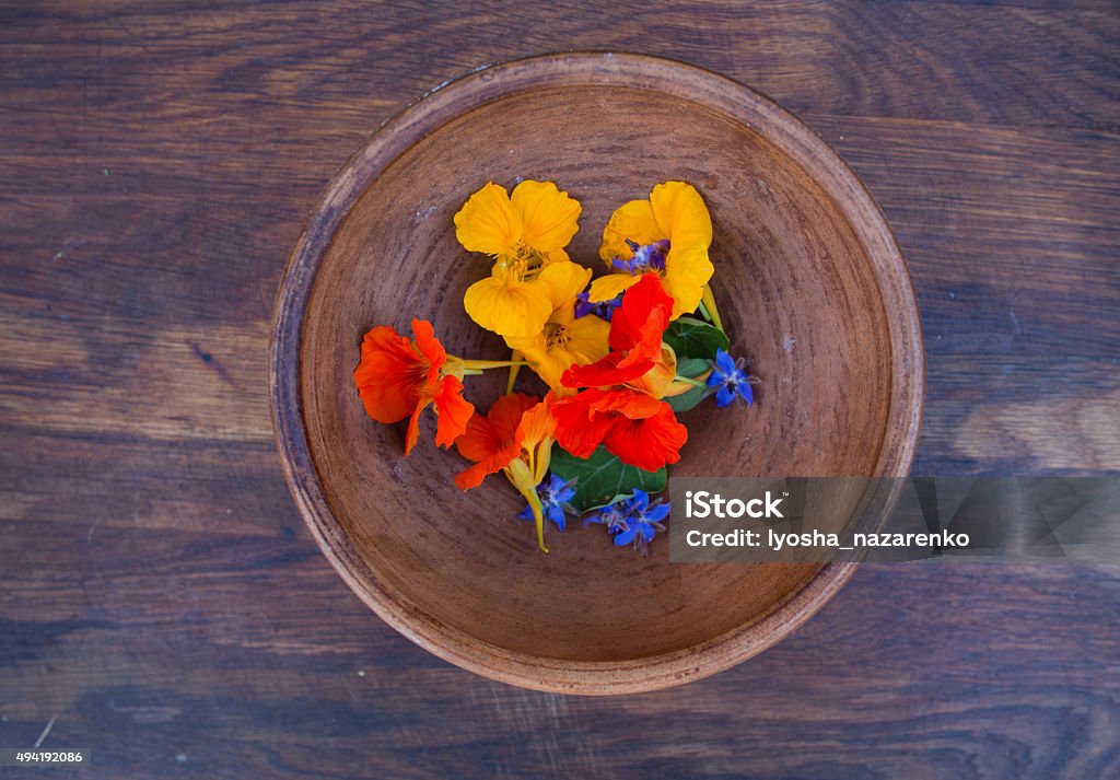 Colorful edible flowers in clay bowl on wooden background Colorful edible flowers in clay bowl on wooden background. Bright nasturtium flowers with leaves and borage. Healthy organic food. Edible Flower Stock Photo