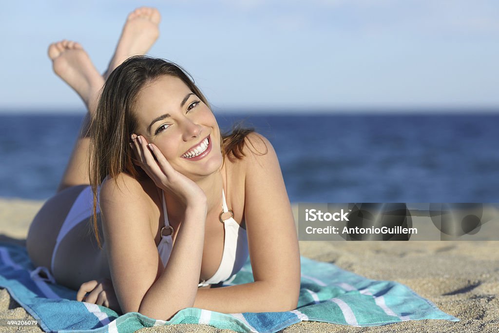 Happy woman with white perfect smile resting on the beach Happy woman with white perfect smile resting on the sand of the beach and looking at camera Women Stock Photo