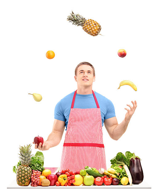 Man juggling with fruits behind a table