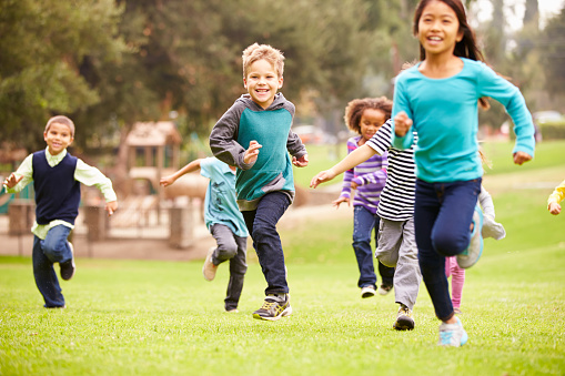 Group Of Young Children Running Towards Camera In Park Smiling To Camera