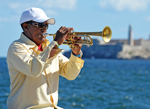 Havana,Cuba, October 31st 2012; A local Cuban musician jams with his trumpet on a sunny morning on the seawall of the Malecon, Havana, with the breakwater of the lighthouse at the entrance to Havana harbour in the distance