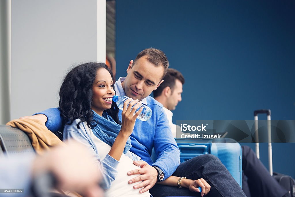 Pregnant woman traveling by plane Happy pregnant woman waiting with her partner for the flight at the airport lounge, drinking mineral water. Pregnant Stock Photo