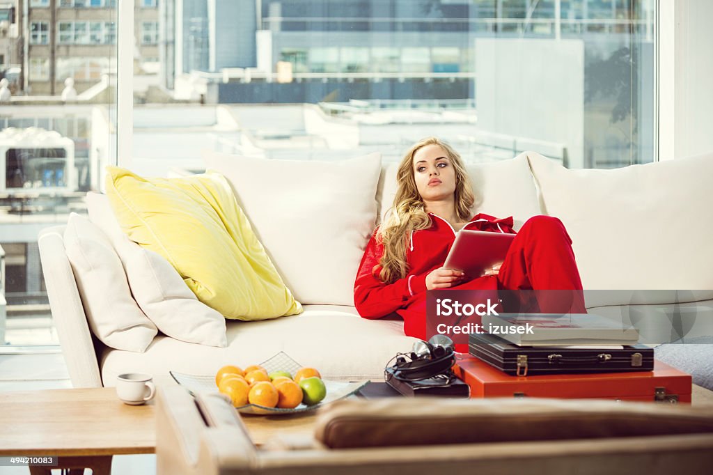 Nostalgia Pensive young woman relaxing on sofa at home, holding digital tablet in hands and looking away. Luxury Stock Photo