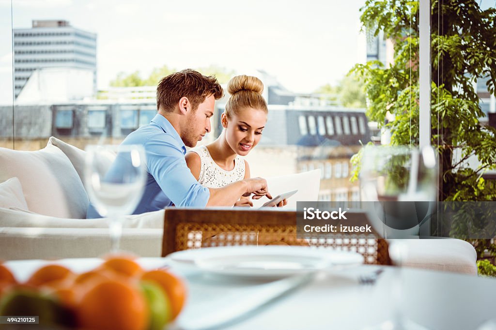 Couple using a digital tablet Young couple sitting on sofa in their penthouse and using digital tablet together. Couple - Relationship Stock Photo