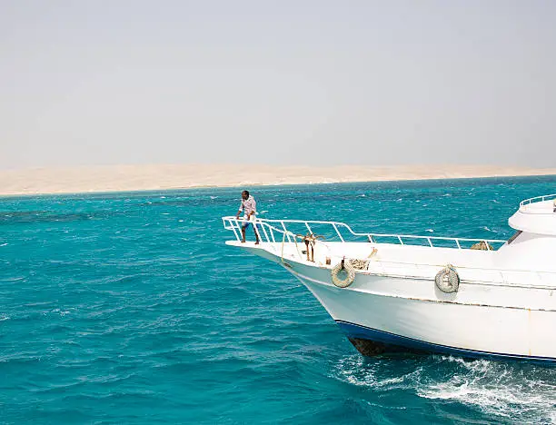 white boat with african black skin fishman on board in red sea egypt sand on background