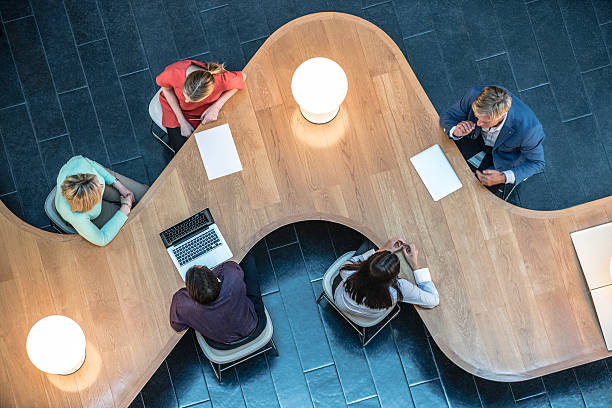 Business people meeting in modern office, view from above. Businessmen and businesswomen sitting at curved desk in meeting. Professional smart office workers sitting at modern table, man using laptop. smart office stock pictures, royalty-free photos & images