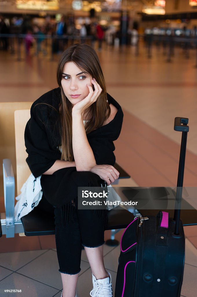 Young female passenger looking sad Airport Young female passenger looking sad at gate waiting in terminal while waiting for her flight. Air travel concept with young casual woman sitting with hand luggage suitcase. 2015 Stock Photo