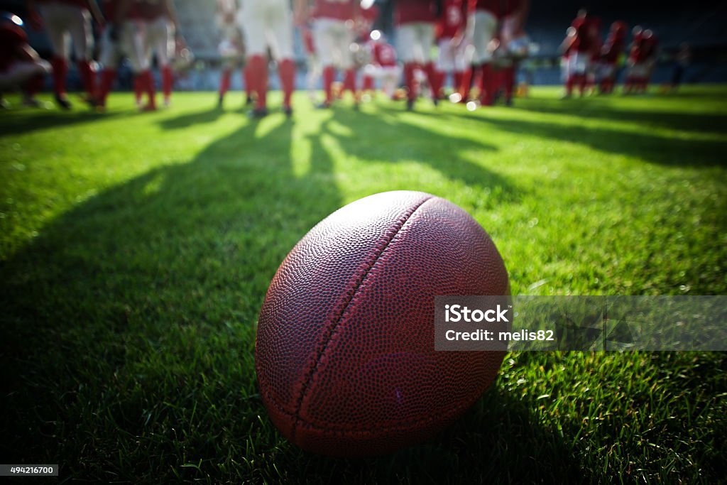 Close up of an american football on the field Close up of an american football on the field, players in the background College American Football Stock Photo