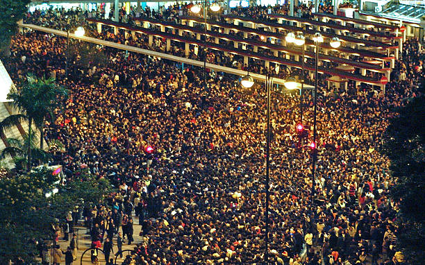 A large nighttime crowd of people gathered near the ferry terminal in Kowloon, Hong Kong.