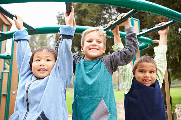 Three Young Boys On Climbing Frame In Playground Three Young Boys On Climbing Frame In Playground Smiling To Camera swing play equipment photos stock pictures, royalty-free photos & images