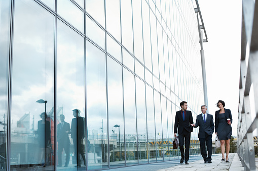 Shot of three businesspeople walking and talking next to an office building