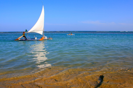 Sailboat crossing water in Northeastern Brazil paradise beach. Porto de Galinhas, Pernambuco State, Brazil.