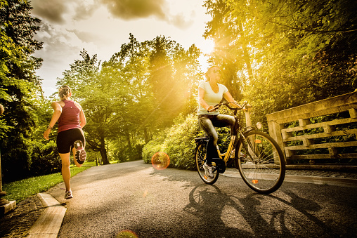Photo of a female cyclist and jogger in the park, with sun flare in the background.