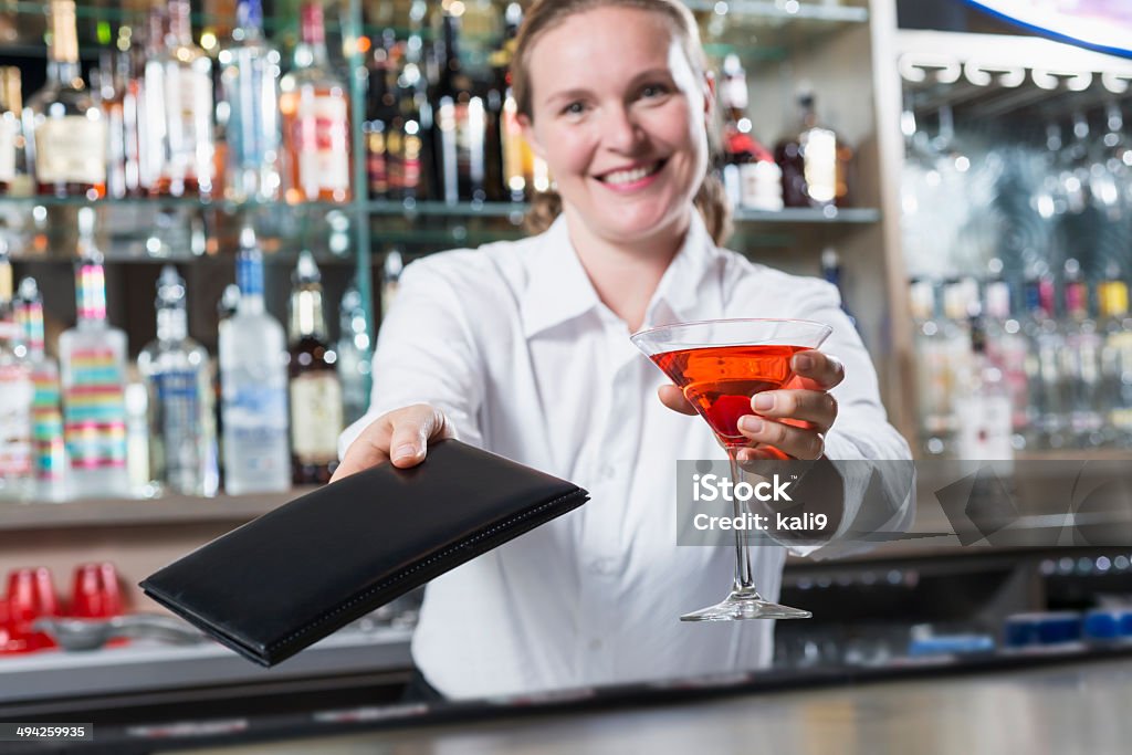 Female bartender Female bartender (30s) serving drink.  Focus on martini and bill. Bartender Stock Photo