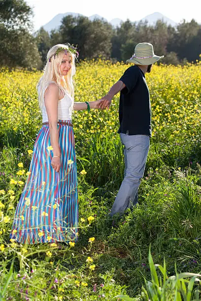 Young man leading his beautiful  young blond girlfriend through a field of colorful yellow rapeseed.