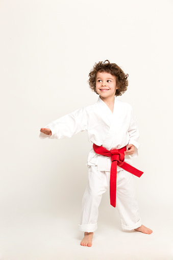 Little boy demonstrates martial art moves wearing Judogi with red belt.