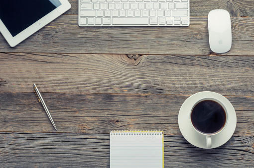 Sydney, Australia - July 27, 2015: Cup of coffee, Apple keyboard and Apple iPad digital tablet on wooden table. The coffee is black. There is also a notepad, pen and Apple computer mouse on the wood surface. High angle view from directly above with copy space. Wood is old and distressed.