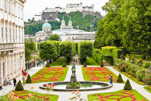 Salzburg, Austria - July 4, 2013: Visitors are walking in beautiful Mirabell Gardens, a castle Hohensalzburg is seen on the background.