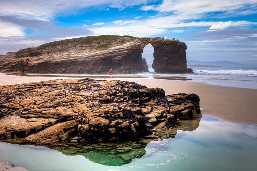 View from the Beach of the Cathedrals ( Playa de Aguas Santas ) and blackened rock on a cloudy and rainy day . Lugo, Galicia, Spain.