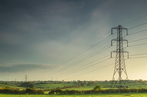Electricity lines carrying power across the countryside of England as the evening sun begins to set.